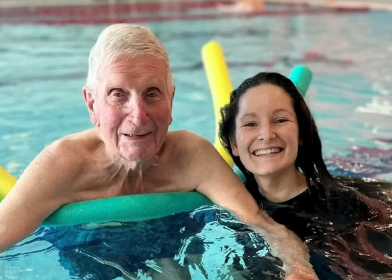 Senior man in pool with assistant